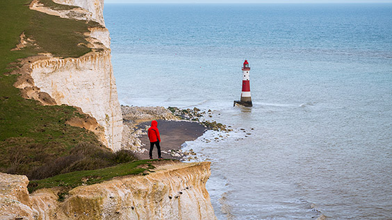 man looking at a lighthouse near a cliff